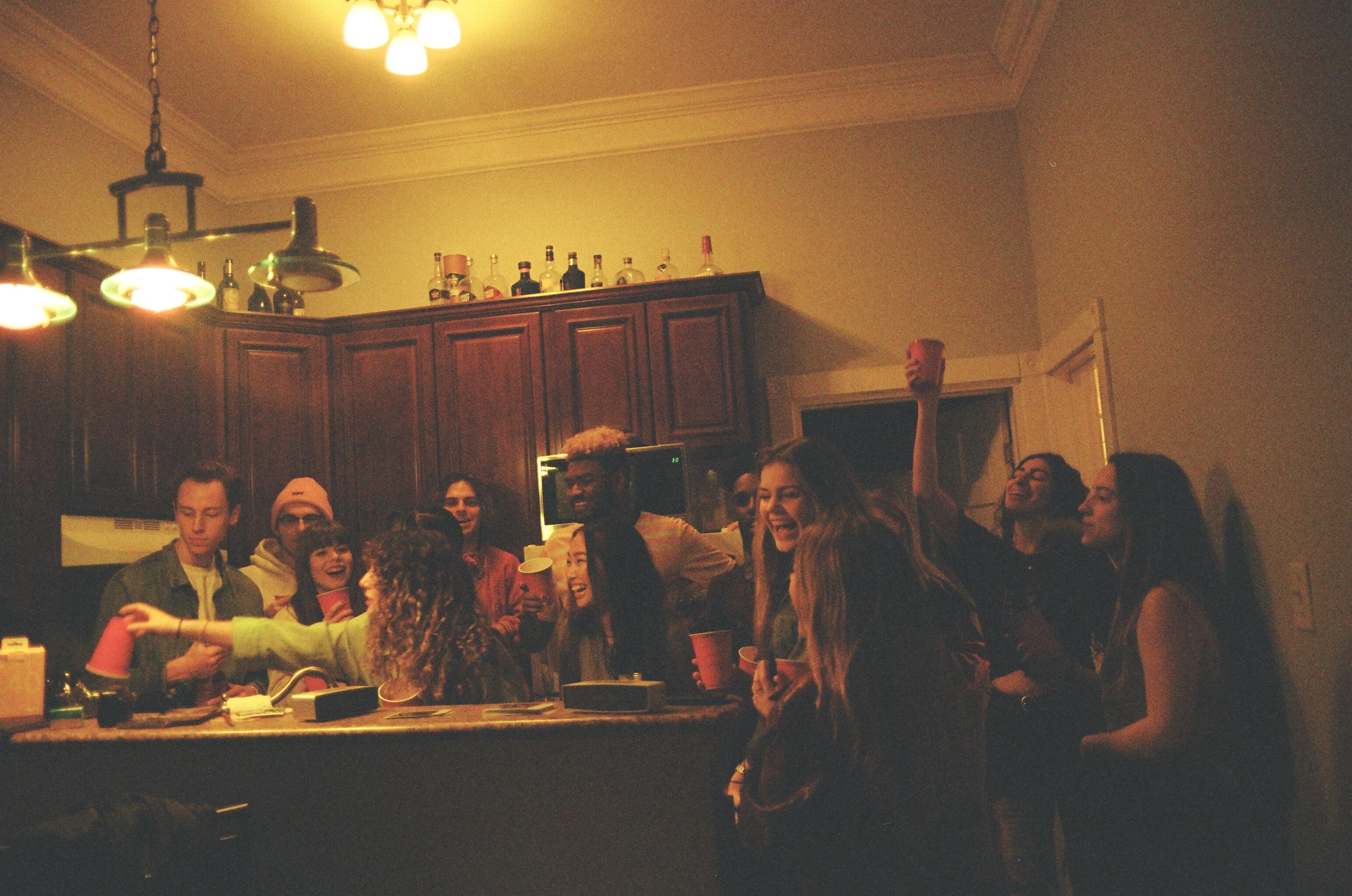 a bunch of young people in a kitchen at a party having drinks