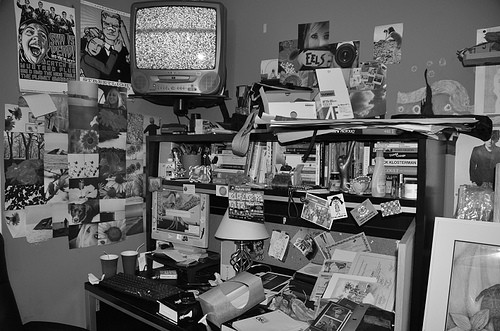 A desk filled with clutter of papers and other items - a television sits on top with static