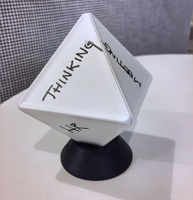 A white, plastic, diamond-like shaped device atop a black circular mount with "Thinking" "Meeting" and "HR" written on it