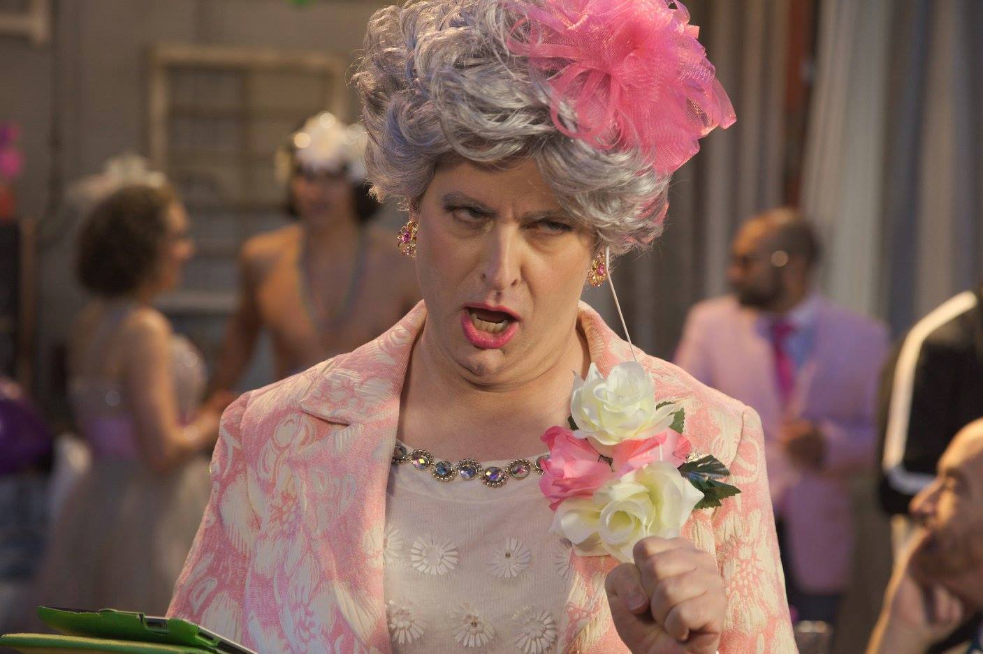 Tyne Firmin as Angry Mama, dressed in drag with pink bonnet and pink blazer