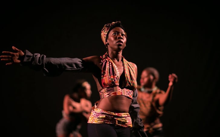 Dance Caribbean COLLECTIVE dancer in the foreground and 2 more in the background, set in black