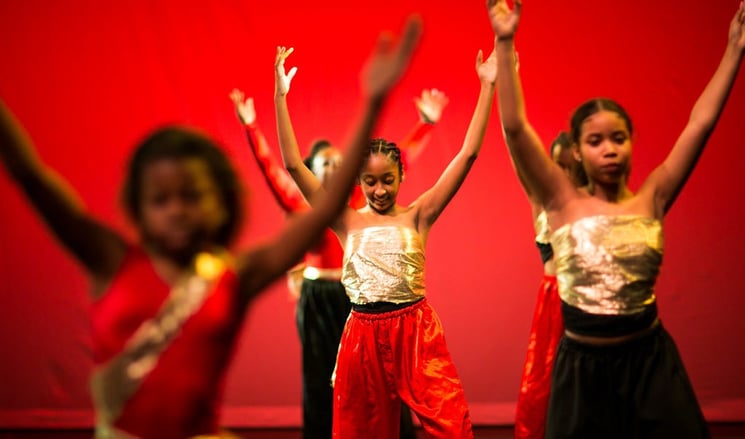 4 girls dancing with arms up in front of red background