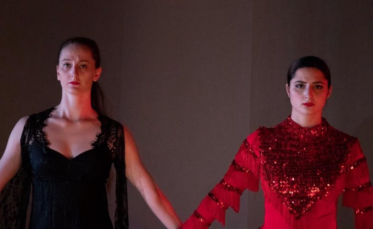 Fluxus Haus performers holding hands, one dressed in red, the other in black