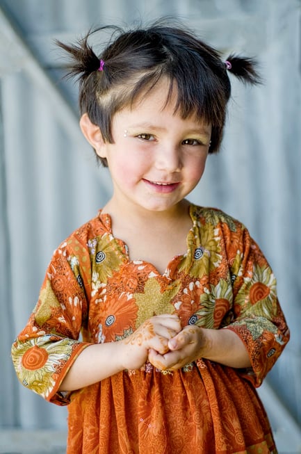 Pashtun kid smiling at camera, hair in little pigtails with rhinestones on face