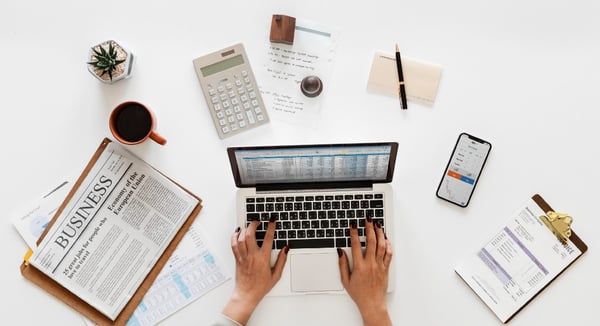 Hands typing on a laptop next to the business section of a newspaper