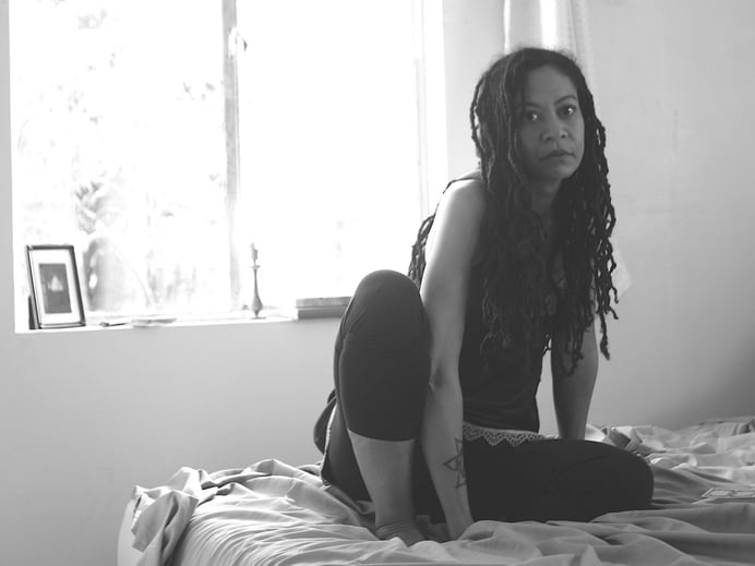 Licity Collins sits on a bed with window in the background, black and white photo