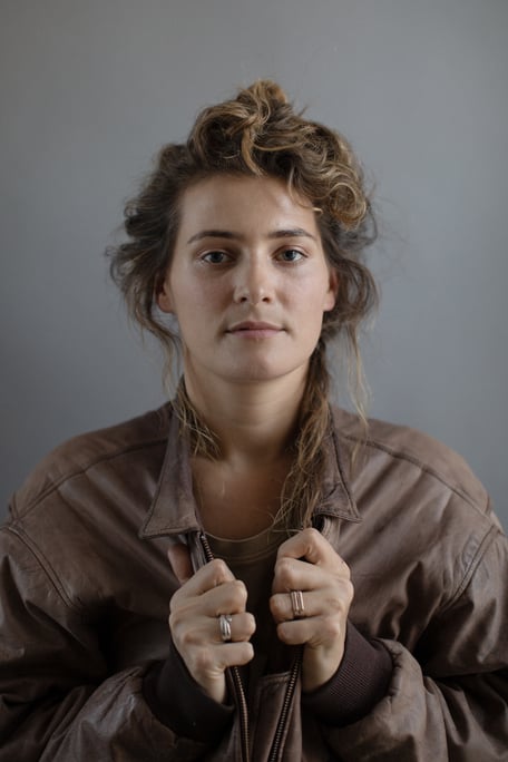 Meryl Jones Williams (Writer & Director) Headshot, in brown leather jacket, holding the lapels