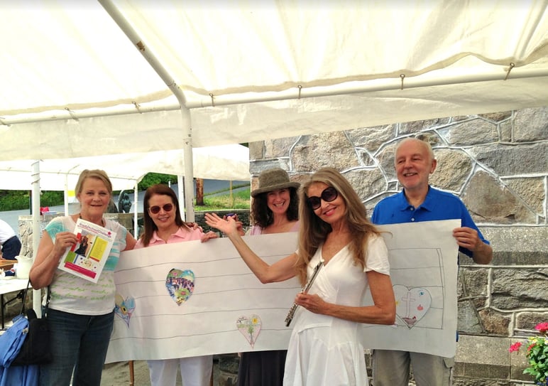 Susan and art project participants smile and hold their artwork