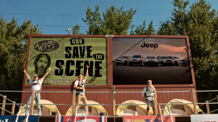 3 performers on stage in front of 2 billboards