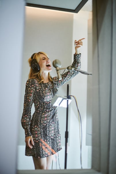 Morgan standing in a studio recording booth singing at the microphone
